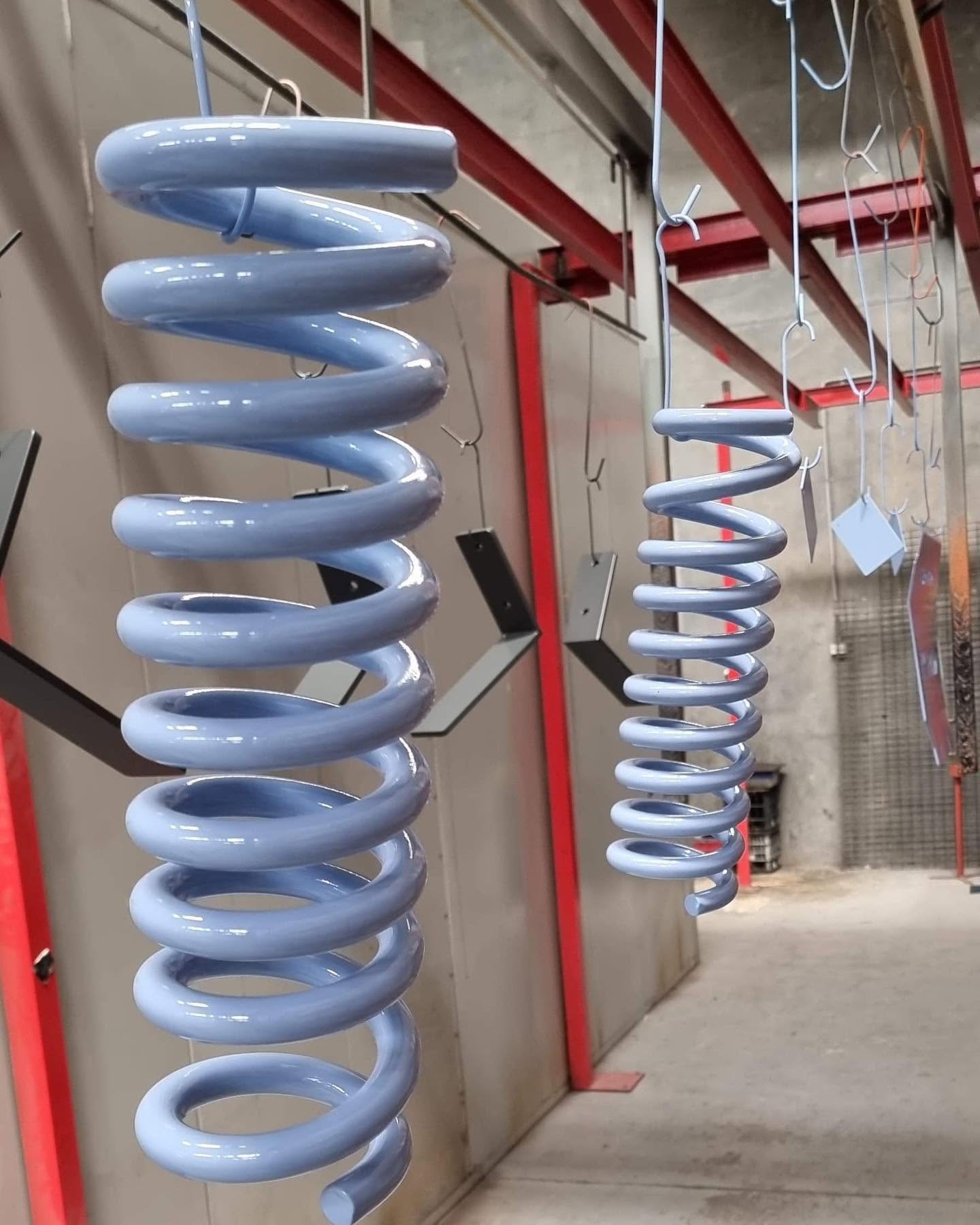 Freshly powder-coated pale blue suspension springs hanging in the 3D Powder Coating workshop