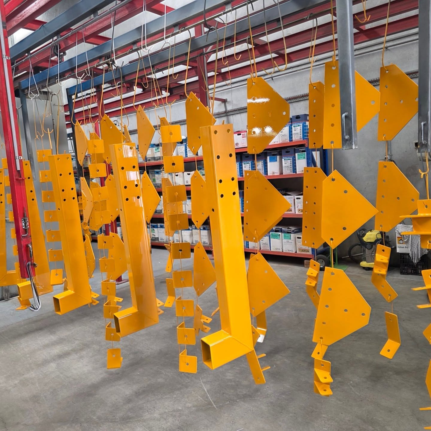 Large batch of bright powder-coated fabricated components hanging from the workshop rail system