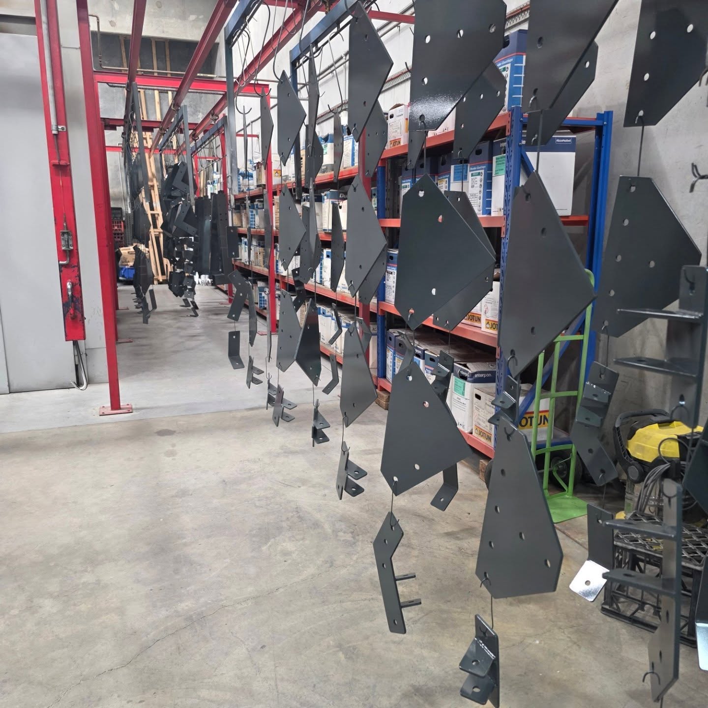 Large dark fabricated components hanging as a coordinated workshop batch