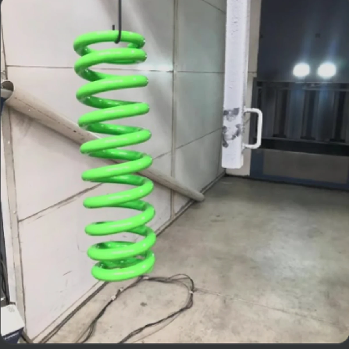 Bright green custom powder-coated coil spring suspended in the workshop