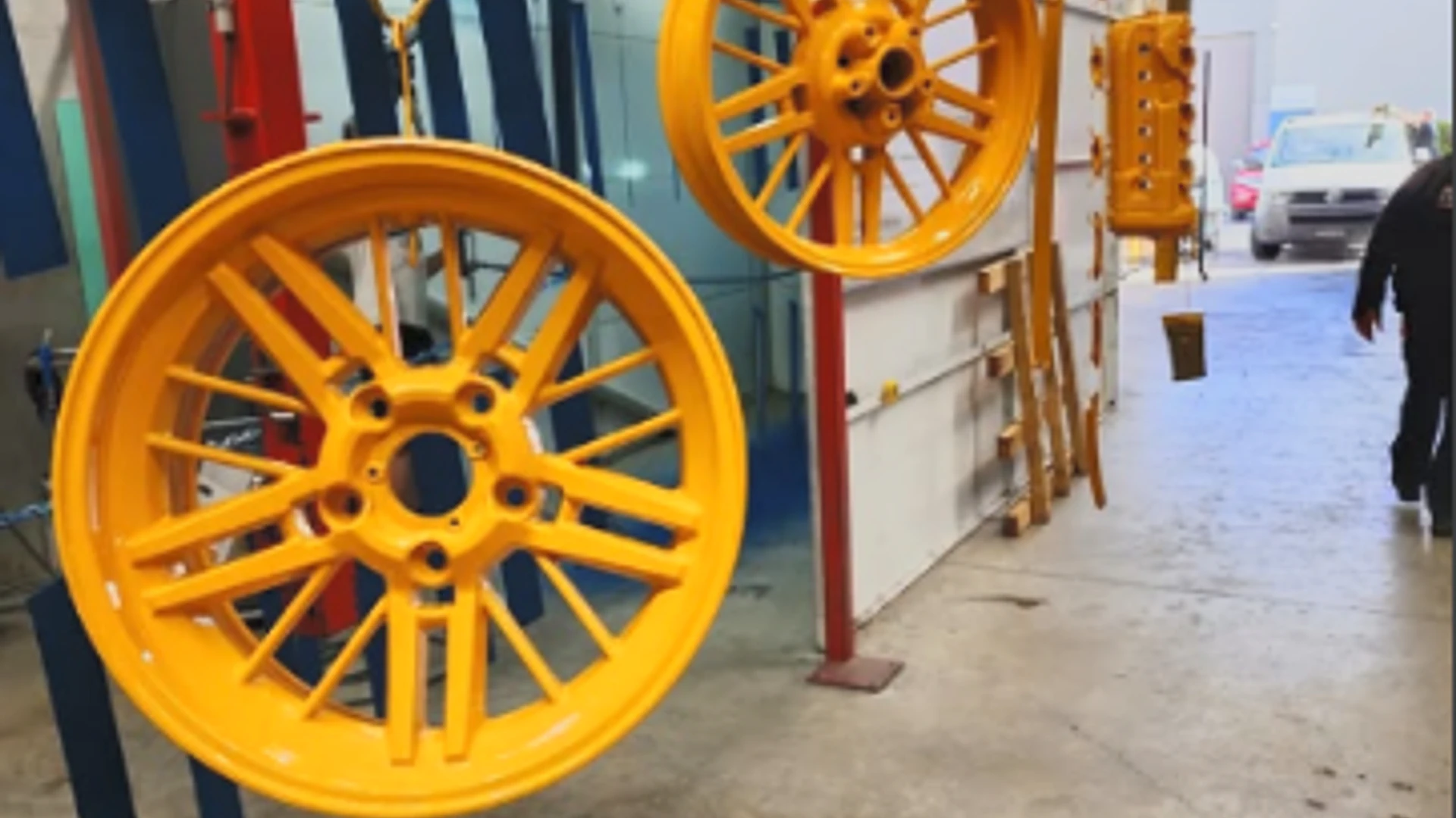 Bright orange powder-coated wheels hanging in the 3D Powder Coating workshop